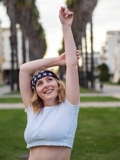Ondiepe focus van een gelukkige blanke vrouw in een trendy bandana en crop top poseren in een park