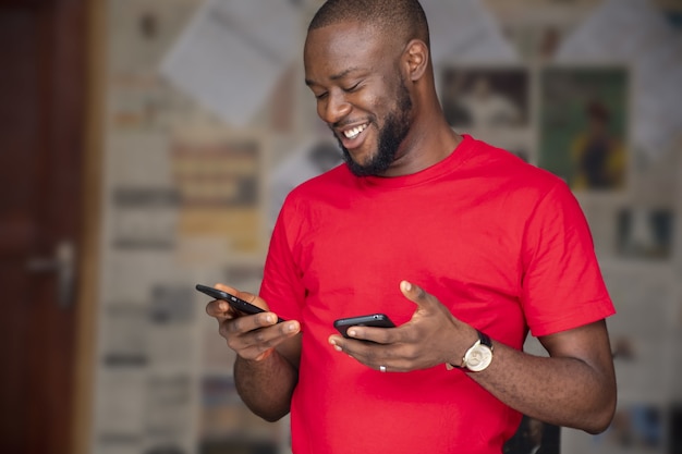 Ondiepe focus van een jonge afrikaanse man die twee telefoons in een kamer gebruikt