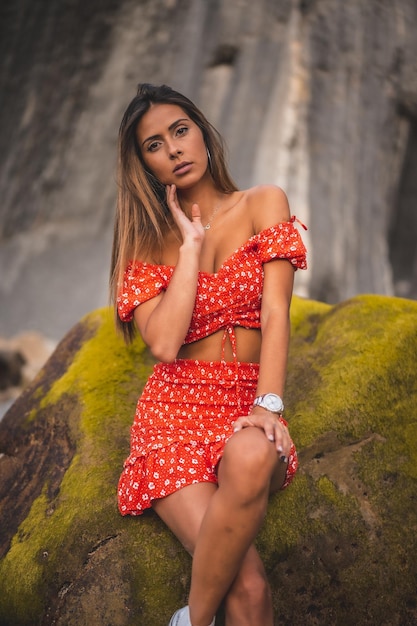 Ondiepe focus van een jonge vrouw met lang haar, gekleed in een rode jurk en poserend bij de rotsen
