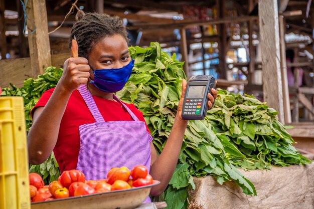 Ondiepe focus van een vrouw met een gezichtsmasker die een POS-machine vasthoudt op een markt