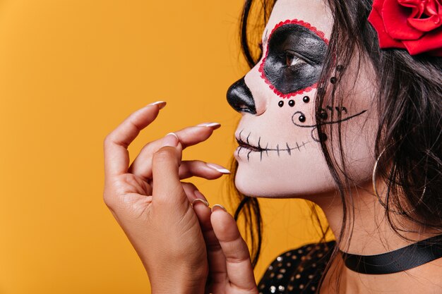 Ongebruikelijk schot van jonge donkerharige vrouw in profiel. Latina-model met sierlijke vingers vormt voor Halloween-foto