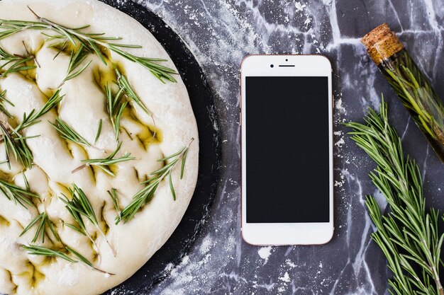 Ongekookt brooddeeg met rozemarijn en smartphone op keukenworktop