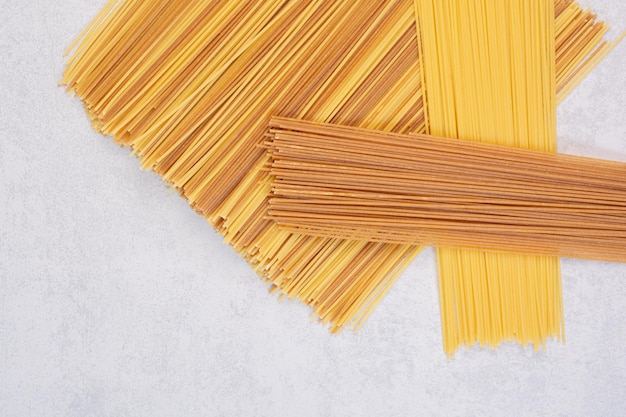 Ongekookte gele en bruine spaghetti op marmeren tafel.