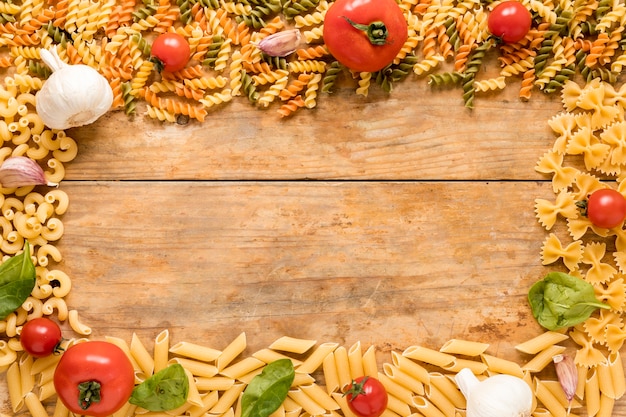 Ongekookte pasta met tomaten; knoflook en basilicum bladeren gerangschikt over gestructureerde oppervlak