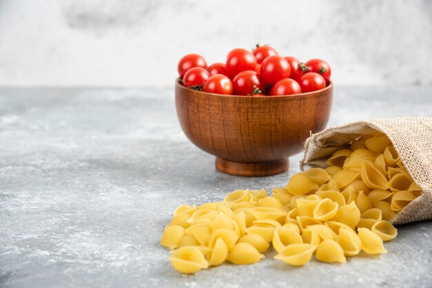 Ongekookte pasta's in een rustieke zak met kerstomaatjes op marmeren tafel.