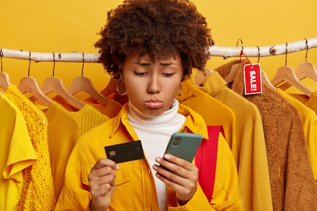 Ongelukkig gekrulde vrouw gebruikt creditcard en smartphone voor online triest winkelen