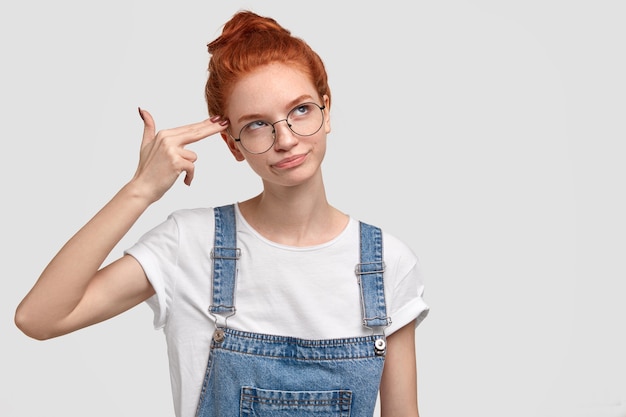 Gratis foto ongelukkig roodharige jonge vrouw imiteert geweerschoten, maakt zelfmoordgebaar, houdt twee vingers op de slapen