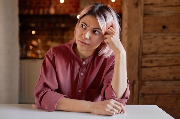 Ongelukkig tienermeisje met roze haar en neusring fronsen, verveeld