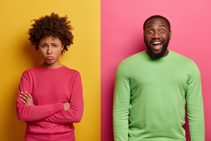 Gratis Foto ongelukkige beledigde vrouw staat met gekruiste armen, praat niet met echtgenoot. vrolijke bebaarde man heeft een donkere huid, giechelt positief om iets grappigs, drukt positieve emoties uit. mensen, reactie