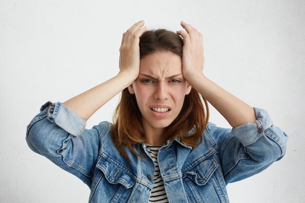 Ongelukkige gefrustreerde vrouw die tanden op elkaar klemt, een pijnlijke blik heeft, grimassen, in de slapen knijpt, lijdt aan migraine of hoofdpijn, zich gestrest voelt