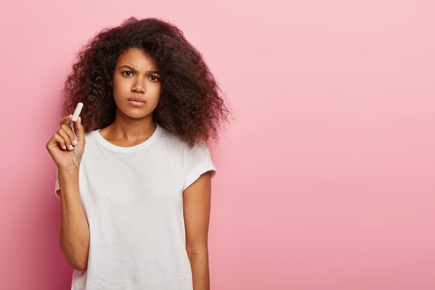 Ongelukkige vrouw met krullend haar houdt schone katoenen tampon vast, verdrietig om menstruatie te hebben