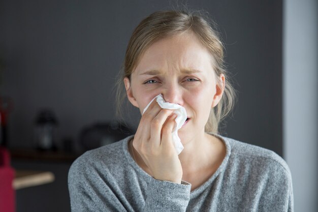 Ongelukkige zieke vrouwen blazende neus met servet, die camera bekijken