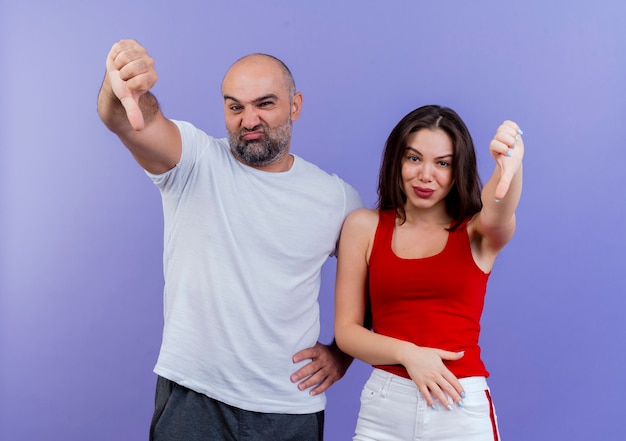 Ongenoegen volwassen paarman die hand op taille houdt en vrouw die hand op buik houdt die zowel duimen naar beneden kijkt als toont