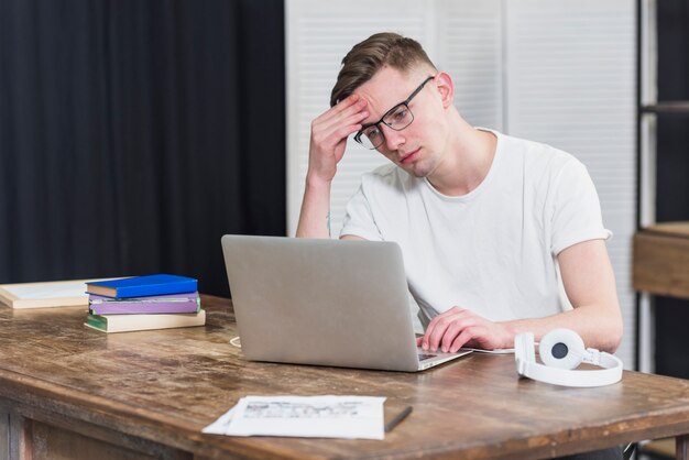 Ongerust gemaakte jonge mens die laptop op houten lijst bekijken