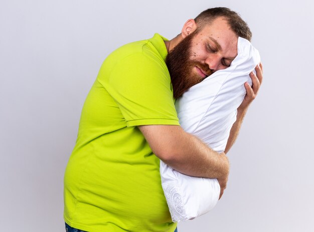 Ongezonde bebaarde man in geel poloshirt voelt zich ziek met kussen en wil slapen met gesloten ogen