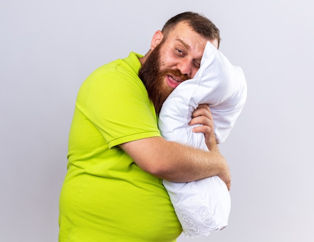 Ongezonde bebaarde man in geel poloshirt voelt zich ziek terwijl hij een kussen vasthoudt dat aan griep lijdt