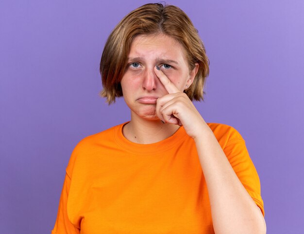 Ongezonde jonge vrouw in oranje t-shirt voelt zich vreselijk huilend hard lijdend aan virus