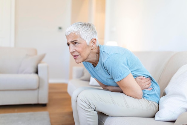 Ongezonde volwassen vrouw met buik gevoel ongemak gezondheidsprobleem concept ongelukkig oudere vrouw zittend op bed lijden aan buikpijn voedselvergiftiging gastritis buikpijn climax