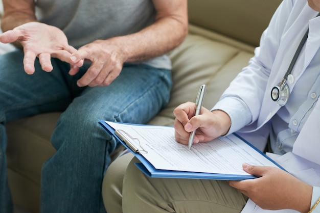 Onherkenbaar arts in gesprek met de patiënt thuis en het maken van aantekeningen