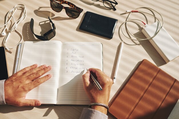 Onherkenbaar man schrijven plan in dagboek en gadgets rondslingeren op het bureau