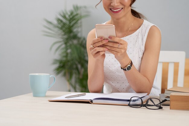 Onherkenbare elegante vrouw zitten aan tafel op het werk en het gebruik van smartphone