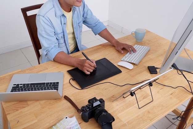 Onherkenbare fotograaf zit aan een bureau en retoucheert foto's op de computer