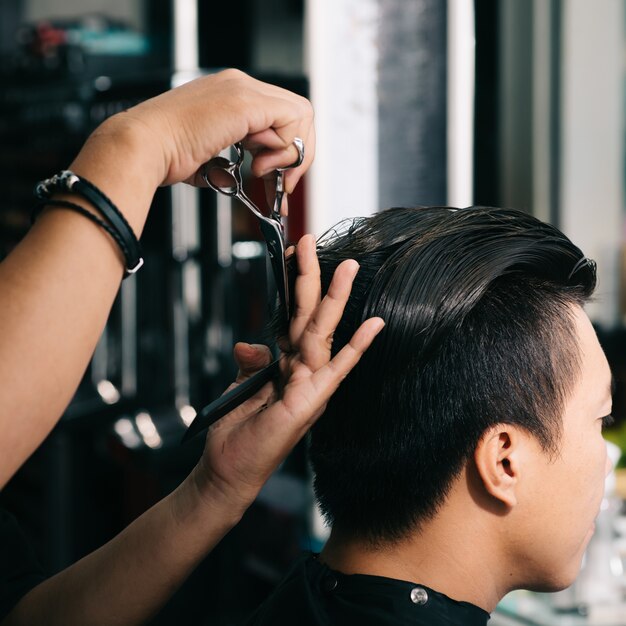 Onherkenbare kapper die het haar van de Aziatische mannelijke klant met schaar in salon snijden