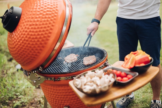 Onherkenbare man die vlees kookt op de grilltafel met gesneden champignons en groenten zomerpicknickfeest