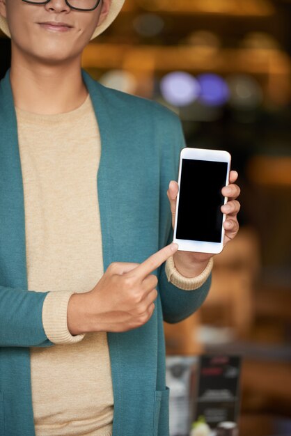 Gratis foto onherkenbare stijlvolle man permanent in café, smartphone houden en wijzend naar het scherm