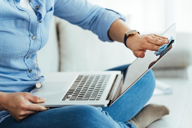 Onherkenbare vrouw die haar laptop thuis schoonmaakt met stoffen doek