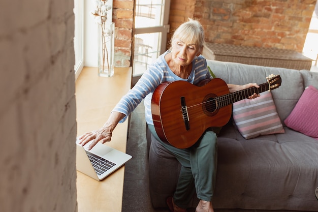 Online gitaar leren spelen. Senior vrouw die thuis studeert, online cursussen krijgt