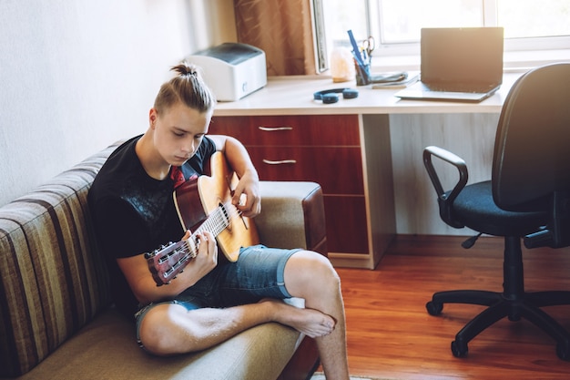 Online gitaarlessen. kaukasische tiener die gitaar speelt, online gitaarlessen heeft, geniet van favoriete hobby, vrije tijd. hoe kies je een gitaar voor een tiener akoestische gitaren voor beginners.