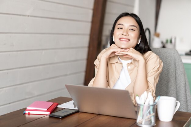 Online onderwijs en werk vanuit huis concept glimlachend Aziatisch meisje zit met laptop en koptelefoon in kit...