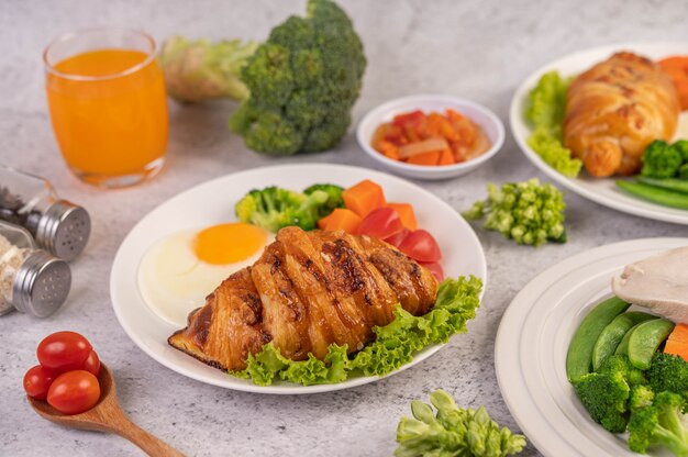 Ontbijt bestaande uit brood, gebakken eieren, broccoli, wortelen, tomaten en sla op een witte plaat.