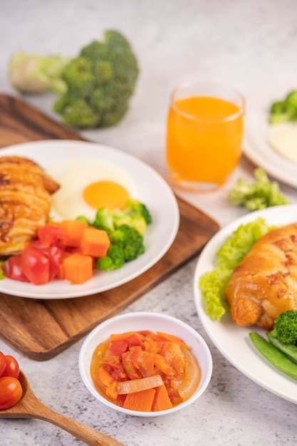 Ontbijt bestaande uit brood, gebakken eieren, broccoli, wortelen, tomaten en sla op een witte plaat.