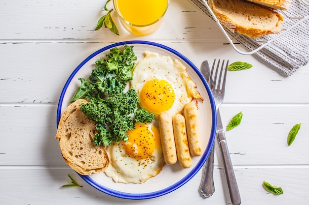 Ontbijt met gebakken eieren, salade, muffins en jus d'orange op witte houten tafel.