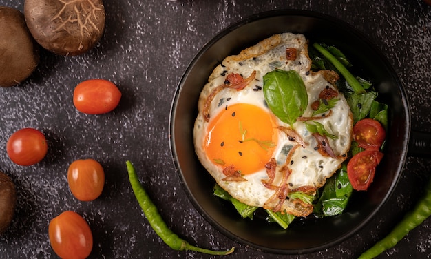 Ontbijt met gebakken eieren, worst en ham in een pan met tomaten. Chili en basilicum
