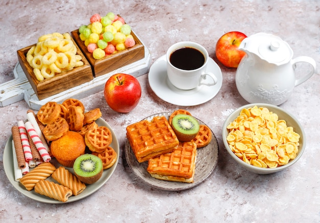 Ontbijt met verschillende snoepjes, wafels, cornflakes en een kopje koffie, bovenaanzicht
