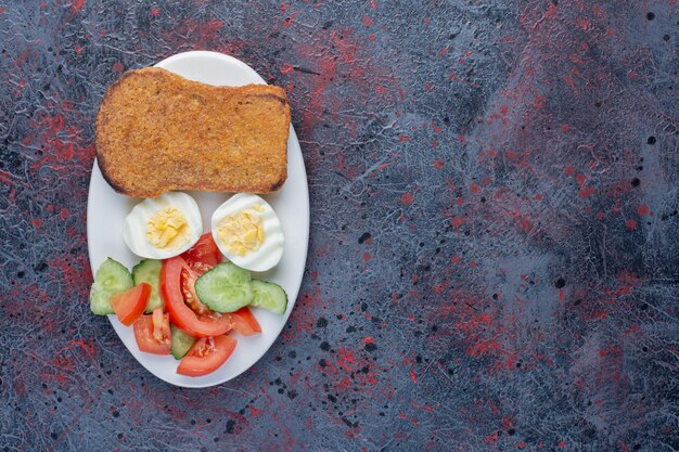 Ontbijtbord met eieren, komkommer en sneetjes brood.