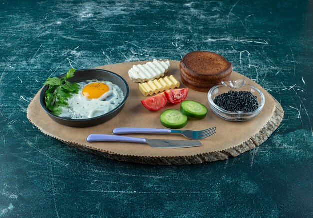 Ontbijtmenu op een houten bord met gebakken ei, kaviaar en pannenkoeken. Hoge kwaliteit foto