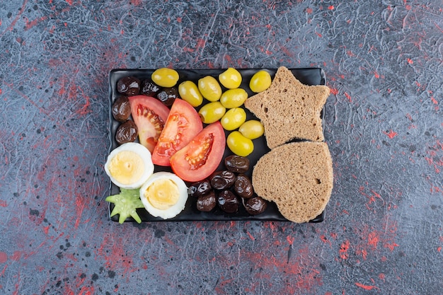 Ontbijtschotel met tomaat, olijven, eieren en brood.