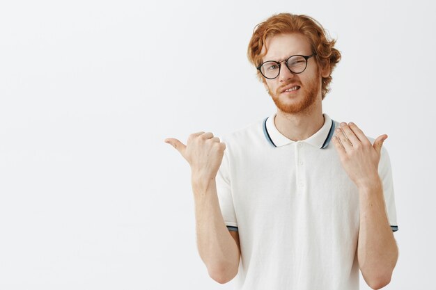 Ontevreden bebaarde roodharige man poseren tegen de witte muur met een bril