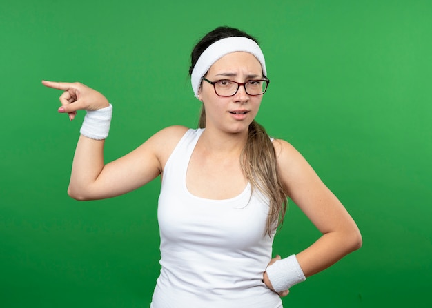 Ontevreden jong sportief meisje met een optische bril met een hoofdband en polsbandjes aan de zijkant