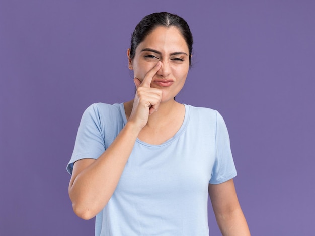 Gratis foto ontevreden jonge brunette blanke meid legt vinger op neus geïsoleerd op paarse muur met kopieerruimte