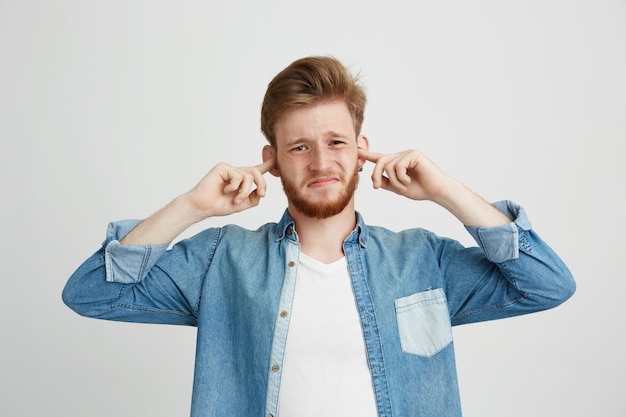 Ontevreden jonge knappe man met baard fronsen sluitende oren.