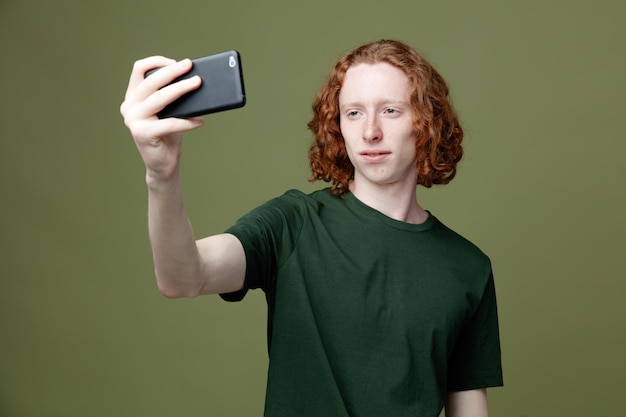 Ontevreden jonge knappe man met een groen t-shirt neemt een selfie geïsoleerd op een groene achtergrond