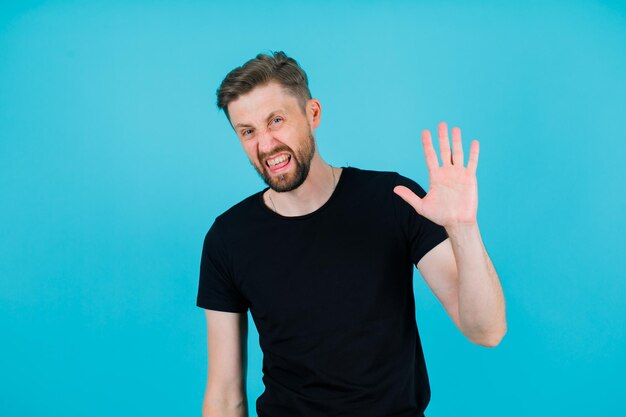 Ontevreden jonge man toont stopgebaar door zijn hand op te steken op een blauwe achtergrond