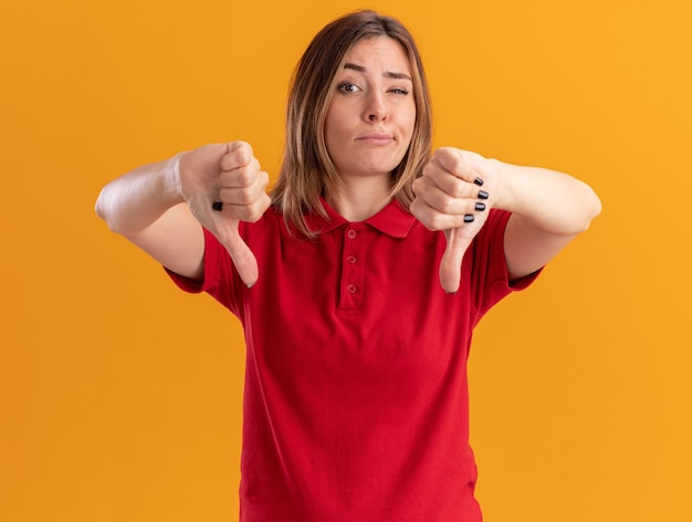 Ontevreden jonge mooie vrouw duimen neer met twee handen geïsoleerd op oranje muur