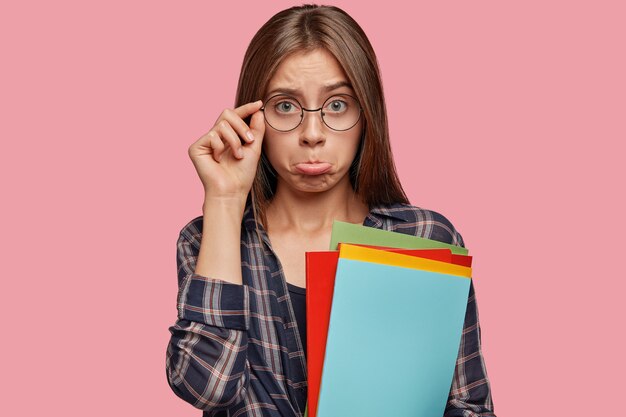 Ontevreden jonge vrouw poseren tegen de roze muur met bril