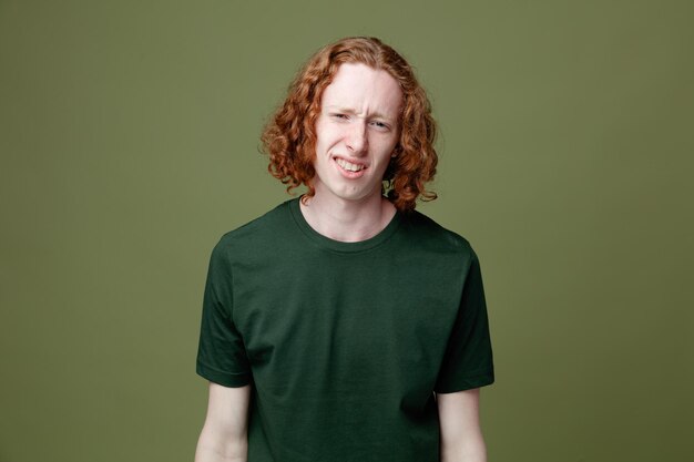 Ontevreden kijken naar camera jonge knappe kerel met groen t-shirt geïsoleerd op groene achtergrond